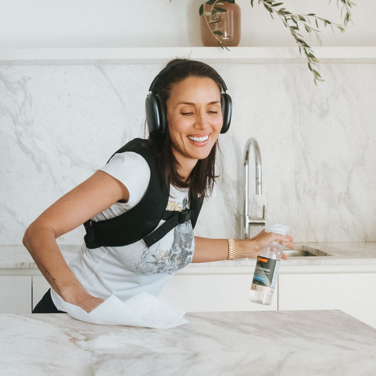 Woman wearing a weighted vest and headphones, cleaning kitchen.